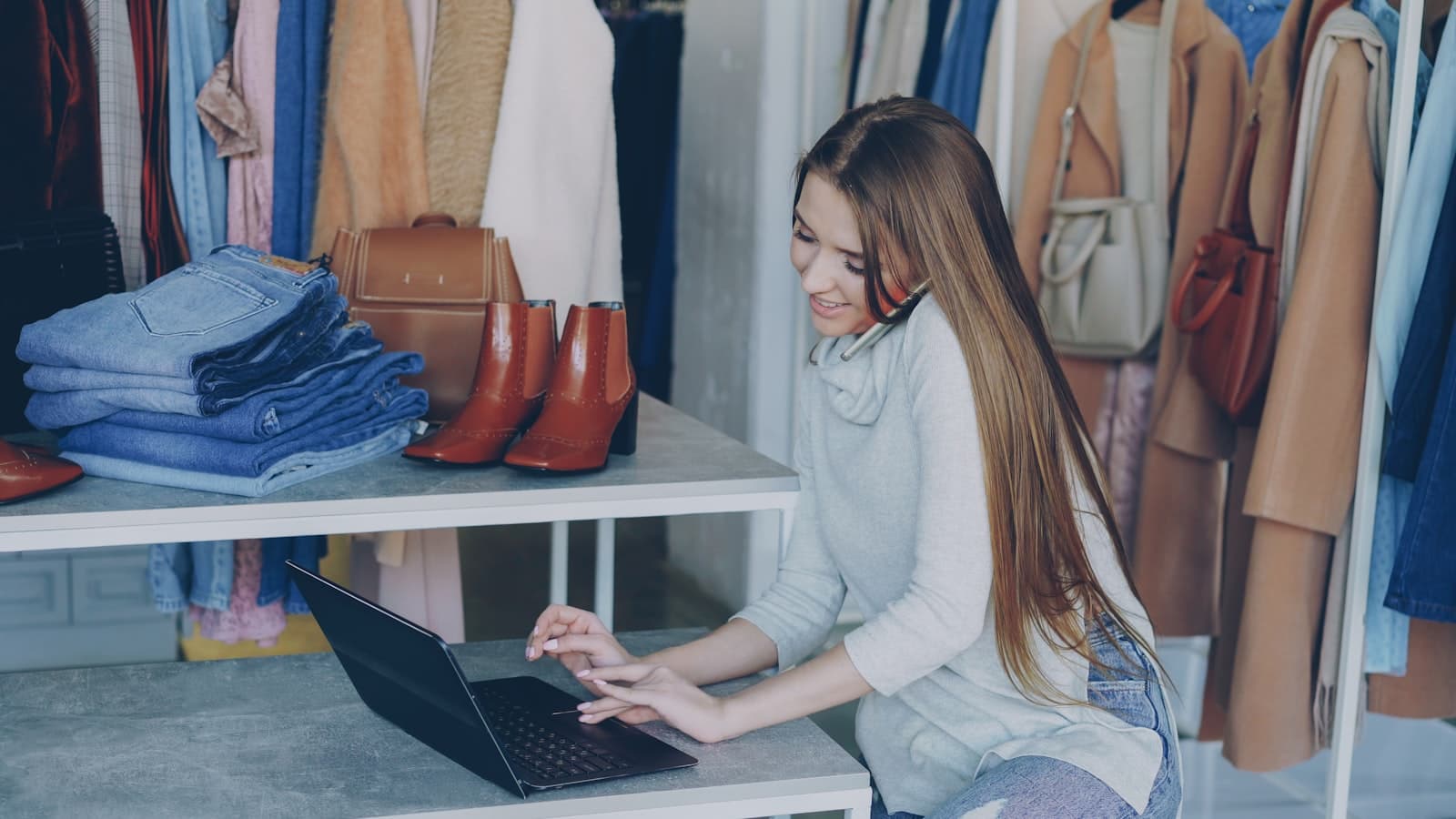 Commerçante indépendante au téléphone devant son ordinateur portable, dans sa boutique de vêtements