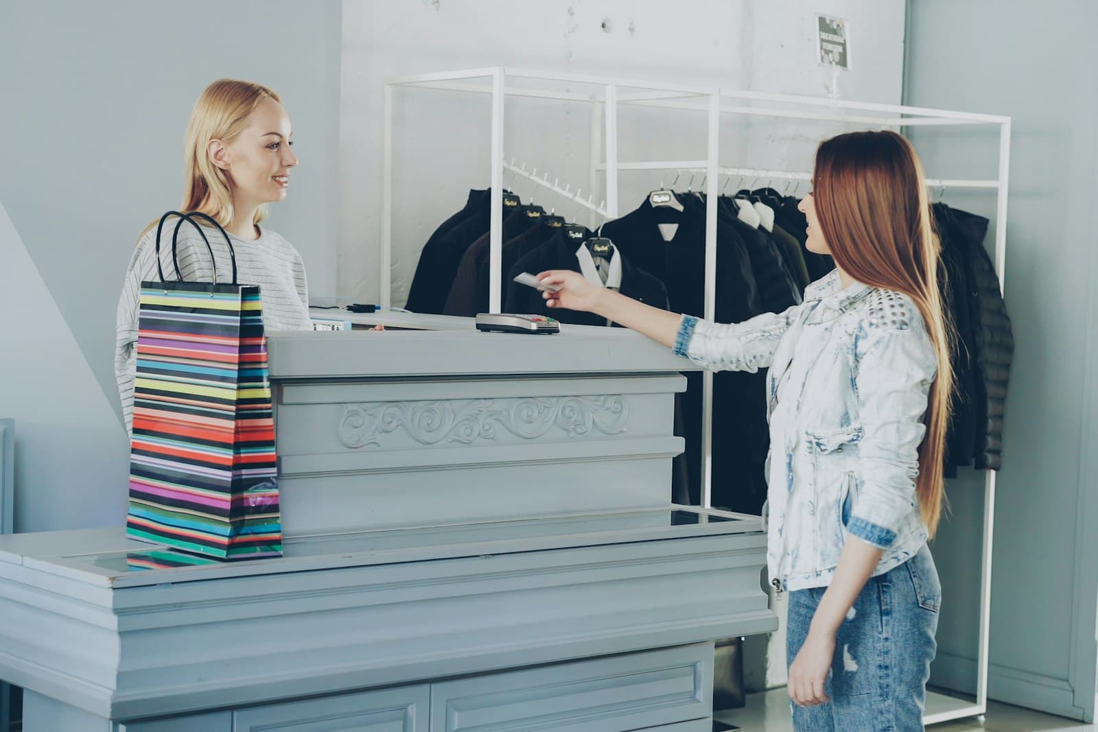 Une cliente règle ses achats par carte au comptoir d'une boutique de vêtements, face à la vendeuse