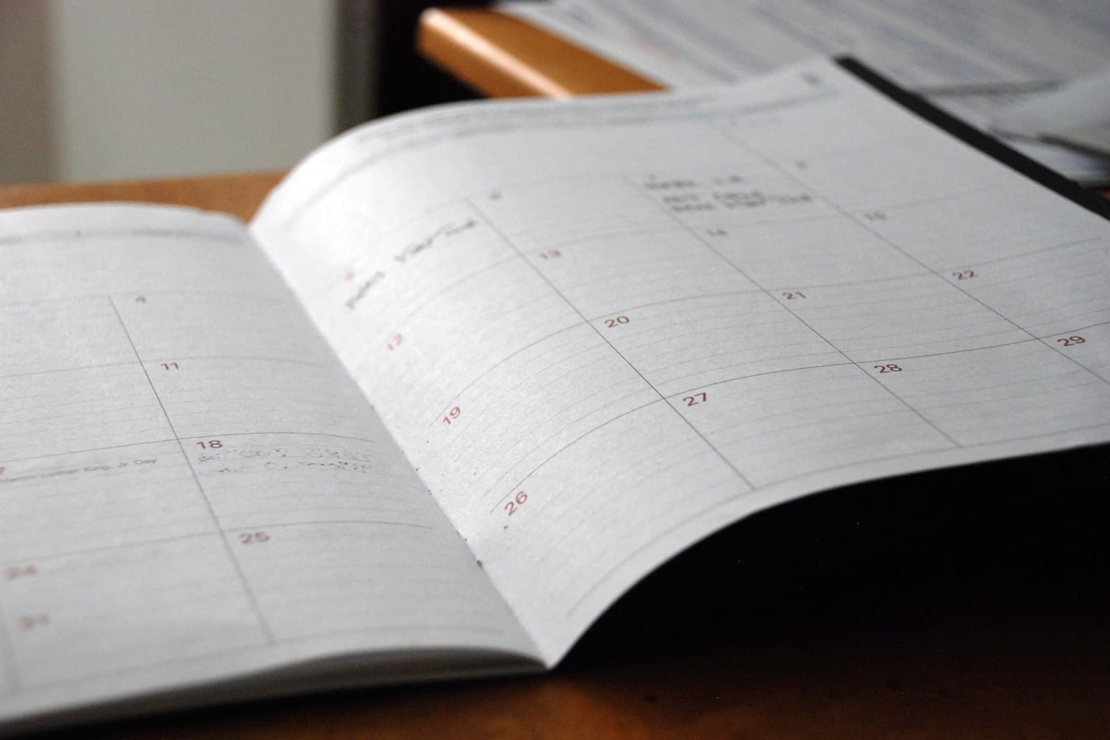 Un agenda papier ouvert sur la page d'un mois, posé sur un bureau en bois