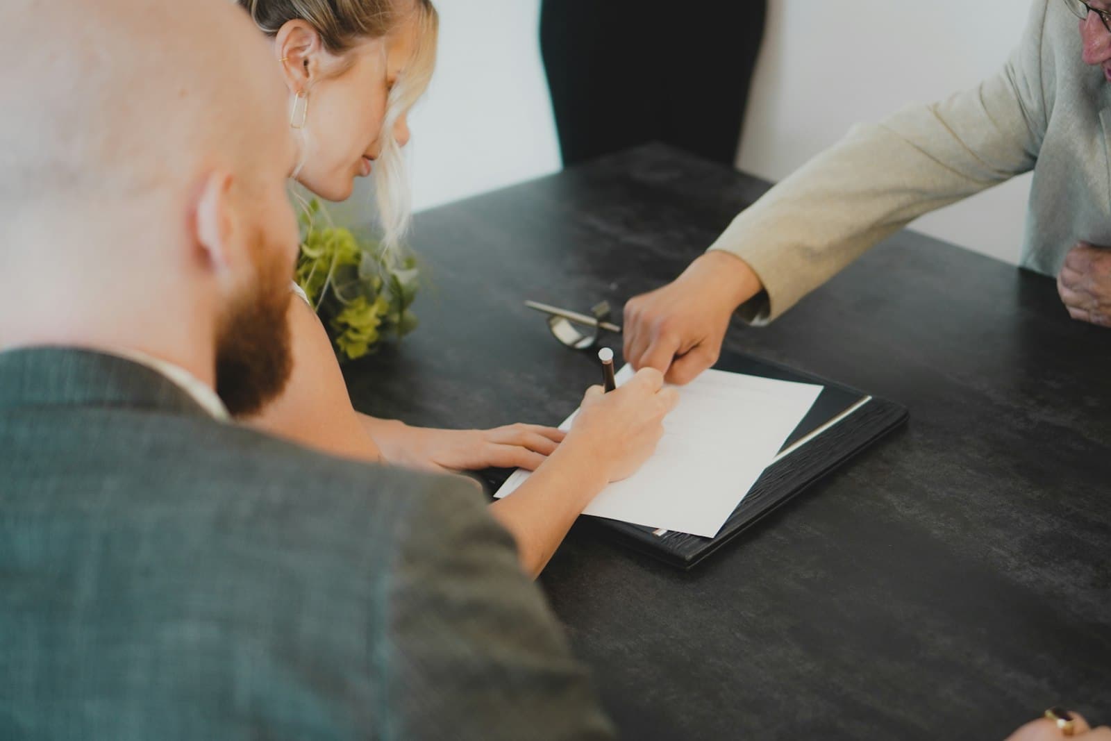 Un couple signe un document sur une table sombre, face à un conseiller qui lui présente le dossier