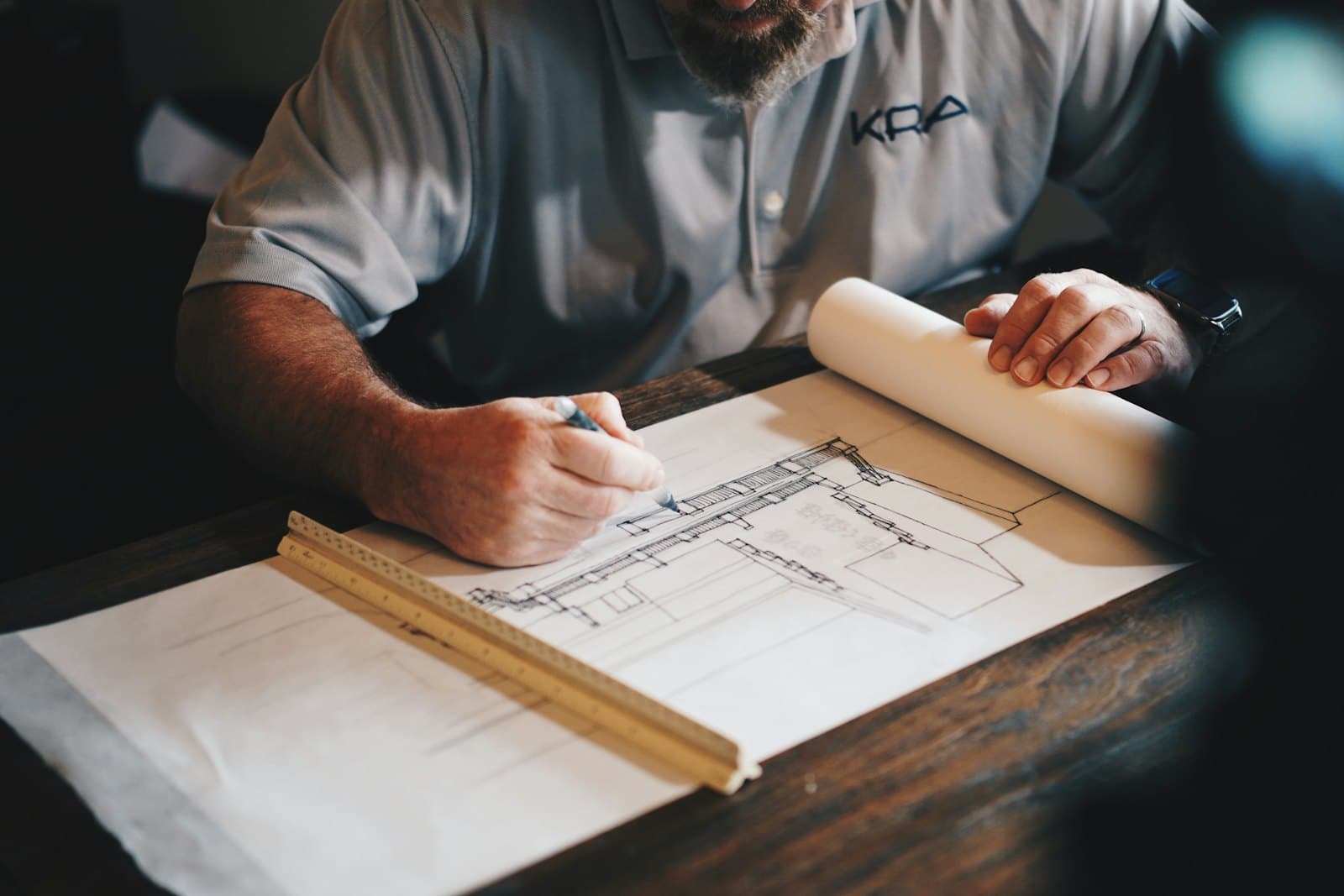 Une personne dessine l'élévation d'un bâtiment au feutre sur un calque, un mètre pliant en bois posé sur la table