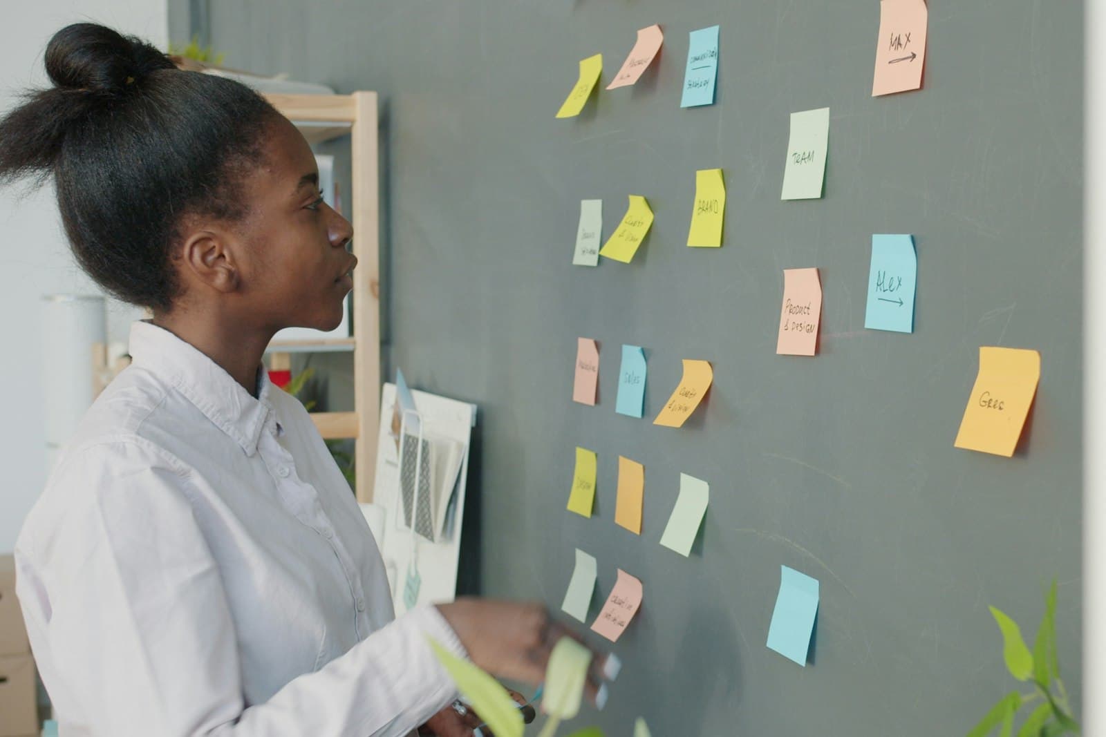 Une femme organise des notes autocollantes de couleur sur un mur d'atelier, formant un tableau de projet fait main