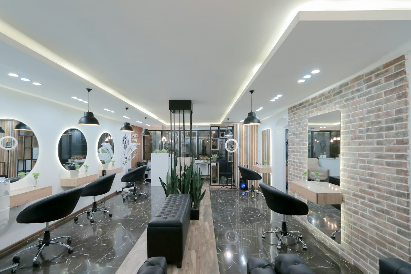 Un salon de coiffure moderne avec des fauteuils noirs, des miroirs ronds éclairés et un mur en briques