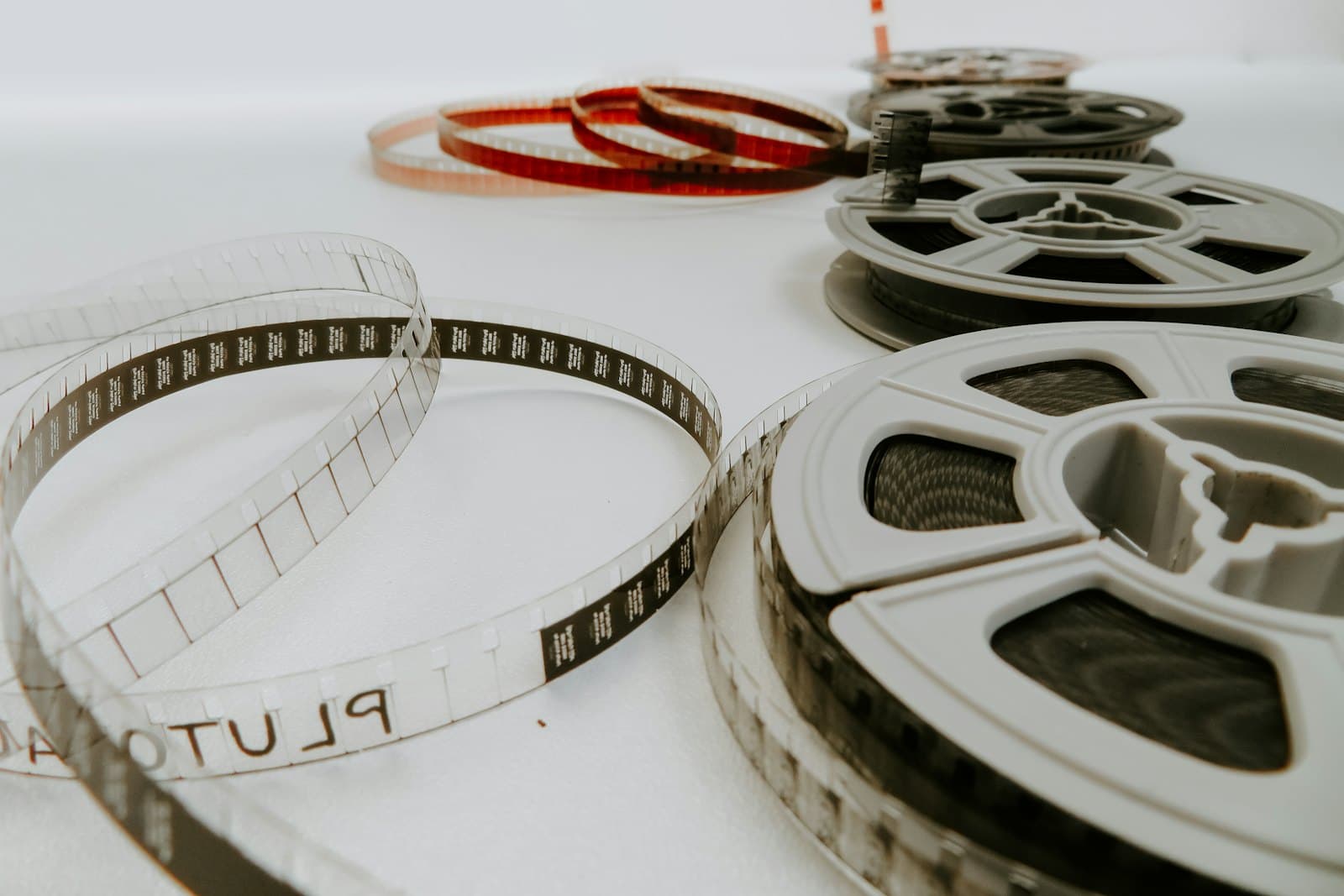 Bobines de film 8 mm en plastique gris posées sur une surface blanche, avec des bandes de pellicule déroulées en boucles