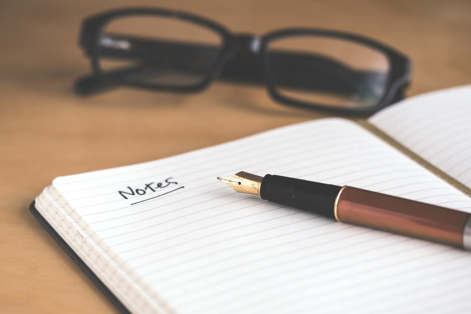Carnet de notes ouvert avec un stylo plume et une paire de lunettes posés sur un bureau